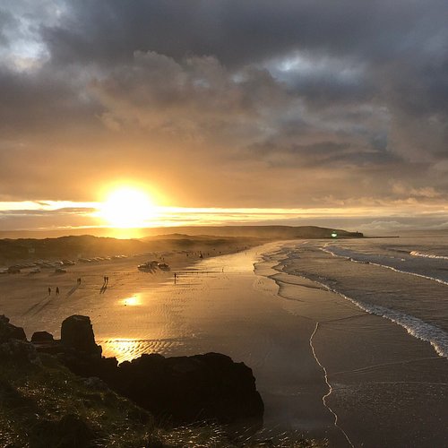 Golden sunset over Portstewart Strand, with waves rolling onto the sandy beach beneath dramatic clouds.